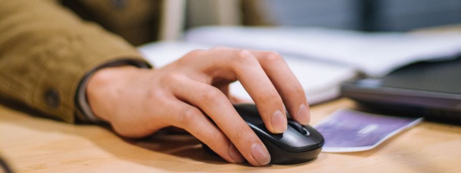 Tecnologia na educação: foto com foco na mão de uma pessoa segurando o mouse de um computador.