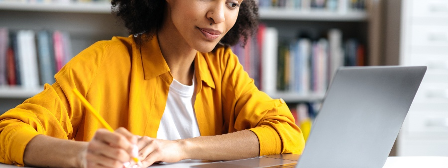 Simulado Enade: fotografia de uma estudante olhando para a tela do computador e anotando em um caderno.