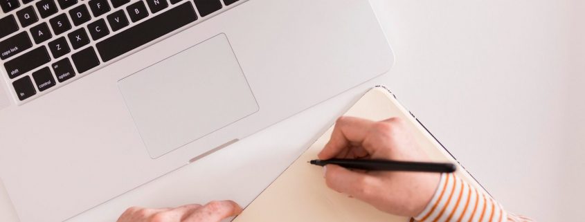 Cursos a distância reconhecidos pelo MEC: fotografia de uma pessoa usando um computador e escrevendo em um caderno.