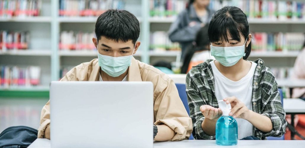 Educação pós-pandemia: fotografia de dois estudantes usando máscaras em uma biblioteca.