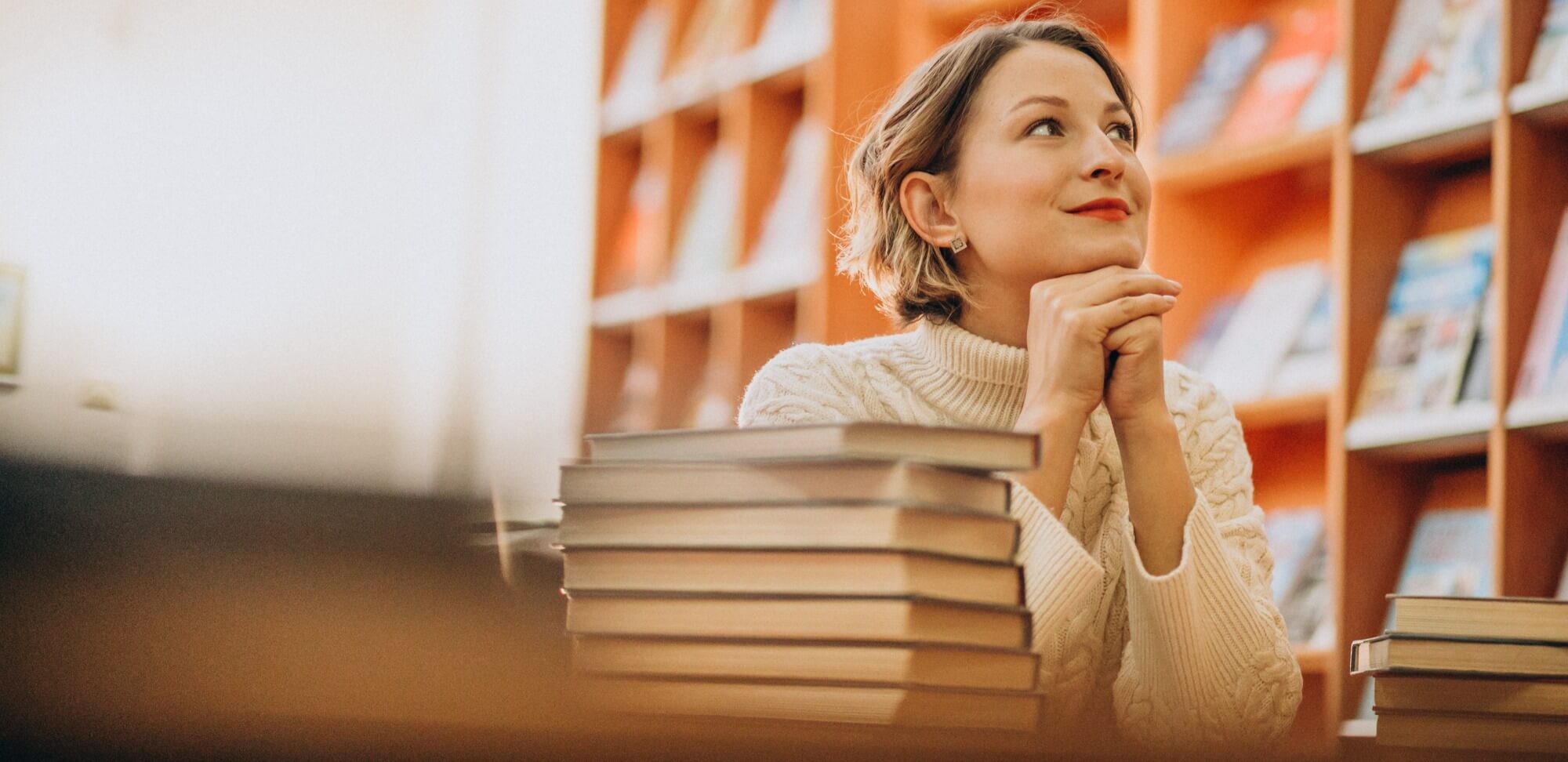 Ranking Enade: fotografia de uma mulher em uma biblioteca, apoiada em uma mesa e olhando para cima.