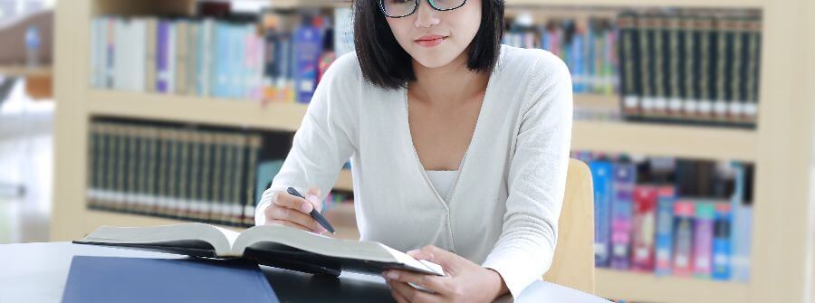 Carga horária do curso de Direito: fotografia de uma estudante lendo um livro em uma biblioteca.