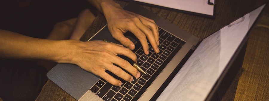Inteligência educacional: fotografia com foco nas mãos de uma pessoa digitando em um computador.