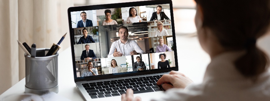Como montar um curso de pós-graduação: fotografia de uma pessoa participando de uma aula online. Na tela do computador, estão aparecendo várias pessoas em uma reunião virtual.