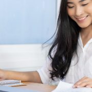 Produção de conteúdo EaD: fotografia de uma mulher sorrindo enquanto estudo com um computador à sua frente e folheia livros.