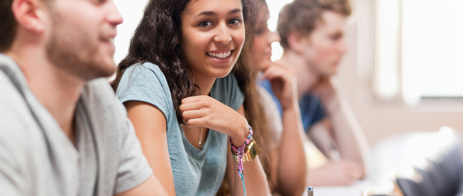Atividades para alunos com dislexia: fotografia e estudantes em uma sala de aula, foco em uma estudante sorrindo para a câmera.