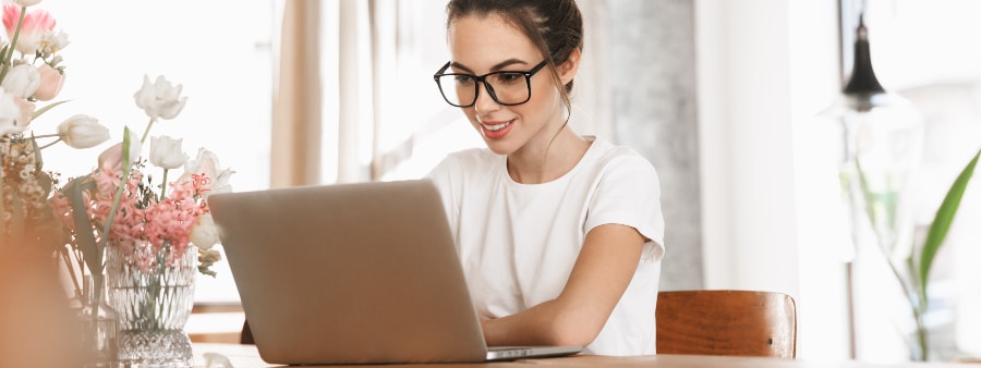 Matrícula online: fotografia de uma mulher de óculos sorrindo enquanto utiliza o notebook.