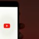 Educação no YouTube: fotografia de uma mão segurando um celular com a marca do YouTube na tela.